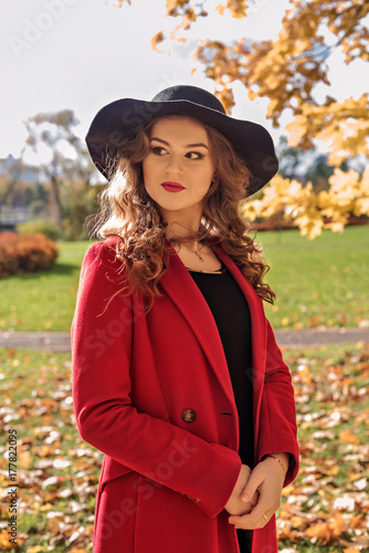 portrait of an aristocratic girl walking in an autumn park in a red coat and a black hat