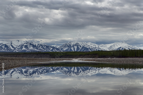Spring mountains with remnants of snow and the reflection in the river. The River Indigirka. Yakutia.