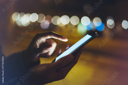 Woman pointing finger on screen smartphone on background illumination bokeh light in night atmospheric city, hipster using in hands mobile phone closeup, glitter street, online wifi internet concept