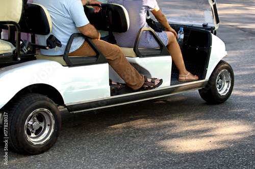 A man and a woman are driving along a road in a park in an electric golf cart. The concept of urban style, ecology, comfort.