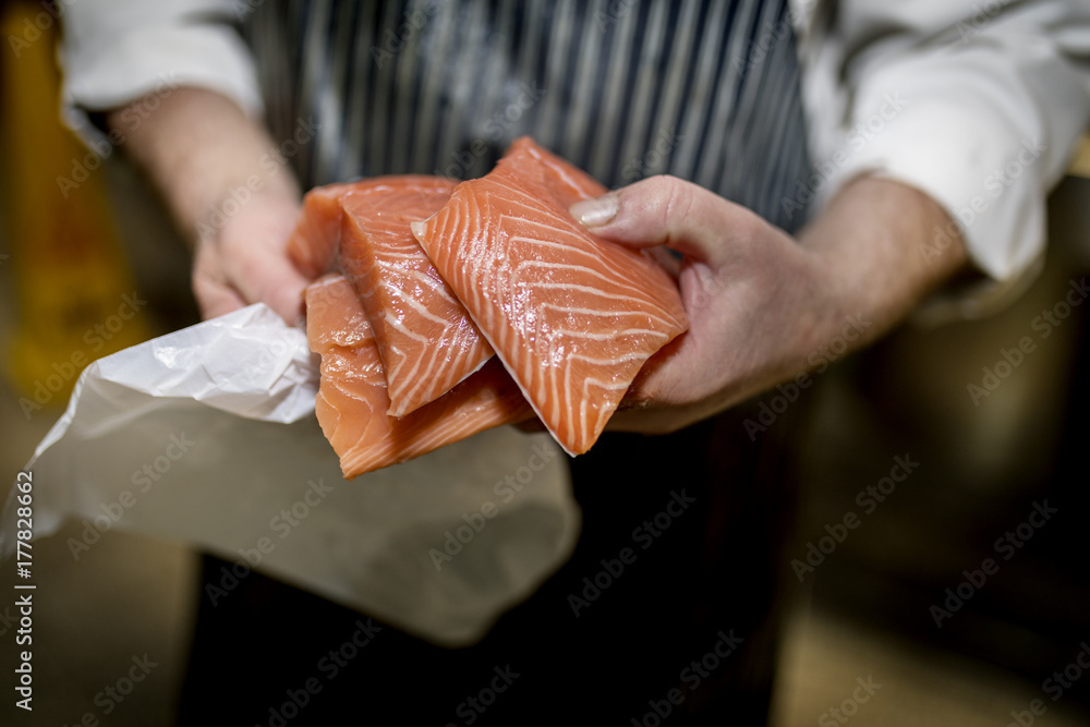 Close up of a fish monger’s hands holding three fillets of fresh filleted salmon on a market stall in Yorkshire, England, UK