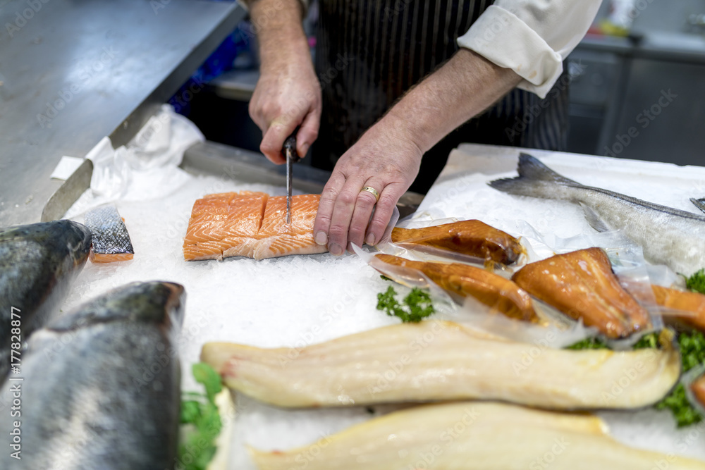 British fish monger slicing, filleting or cutting fresh slamon on ice on a market staff in Yorkshire, England in the UK