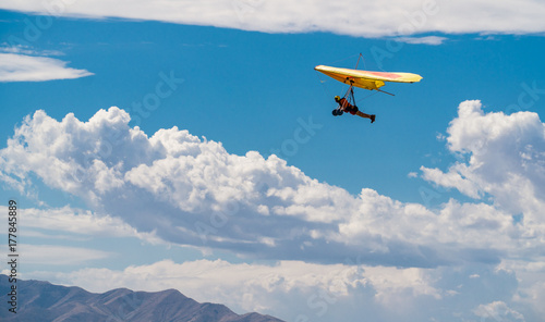 Orange and yellow hang glider in blue sky with clouds