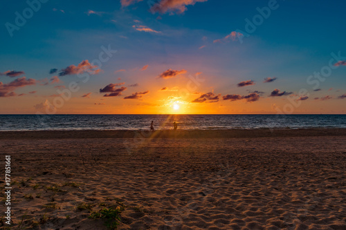 silhouettes of people walking through early morning light rays from the sun shining on a sandy beach