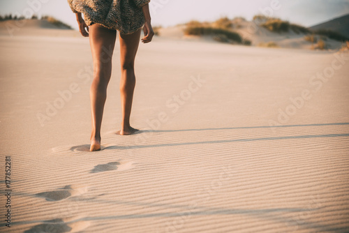 Fototapeta Naklejka Na Ścianę i Meble -  Legs of a young black woman walking in the sand in a desert dunes