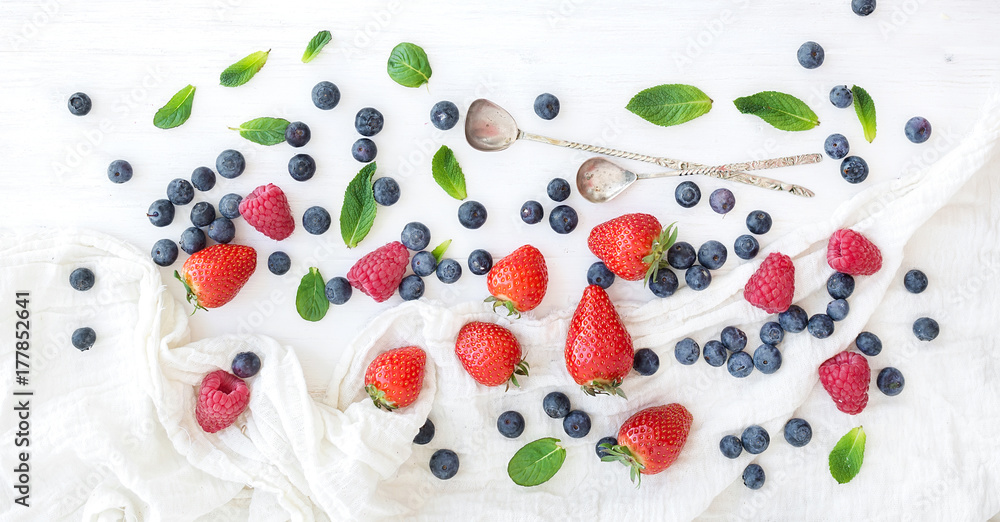 Berry frame with copy space on right. Strawberries, raspberries, blueberries and mint leaves, white wooden background, top view Berry frame with copy space on right. Strawberries, raspberries, blueberries and mint leaves, white wooden background, top view