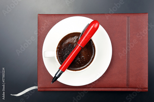 the red pen is on the Cup with black coffee and a notebook