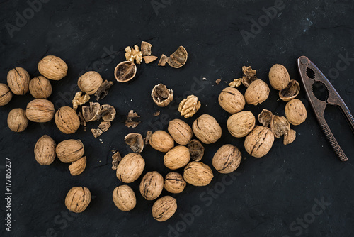 Walnuts with nutcracker over black slate stone background  top view