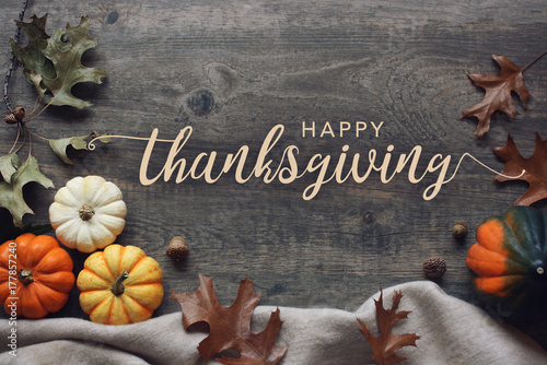 Happy Thanksgiving script with pumpkins and leaves over dark wooden background photo
