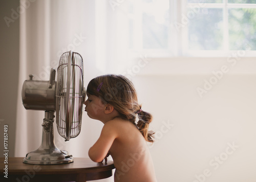 Girl standing in front of retro fan on hot summer day photo