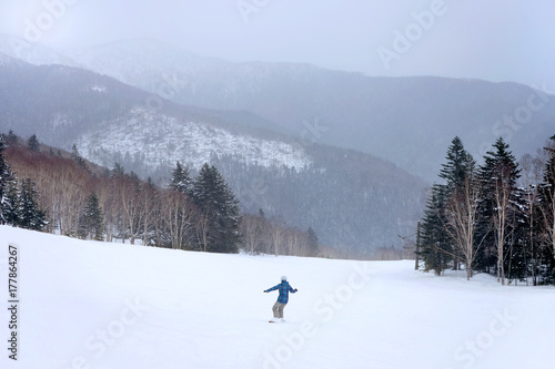 Snowboarder going down the slope at snowy forest resort
