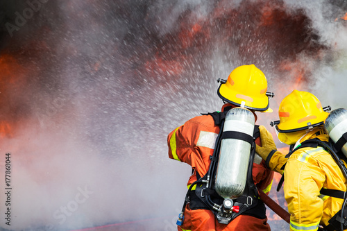 two firefighters water spray by high pressure nozzle to fire surround with smoke and copy space photo