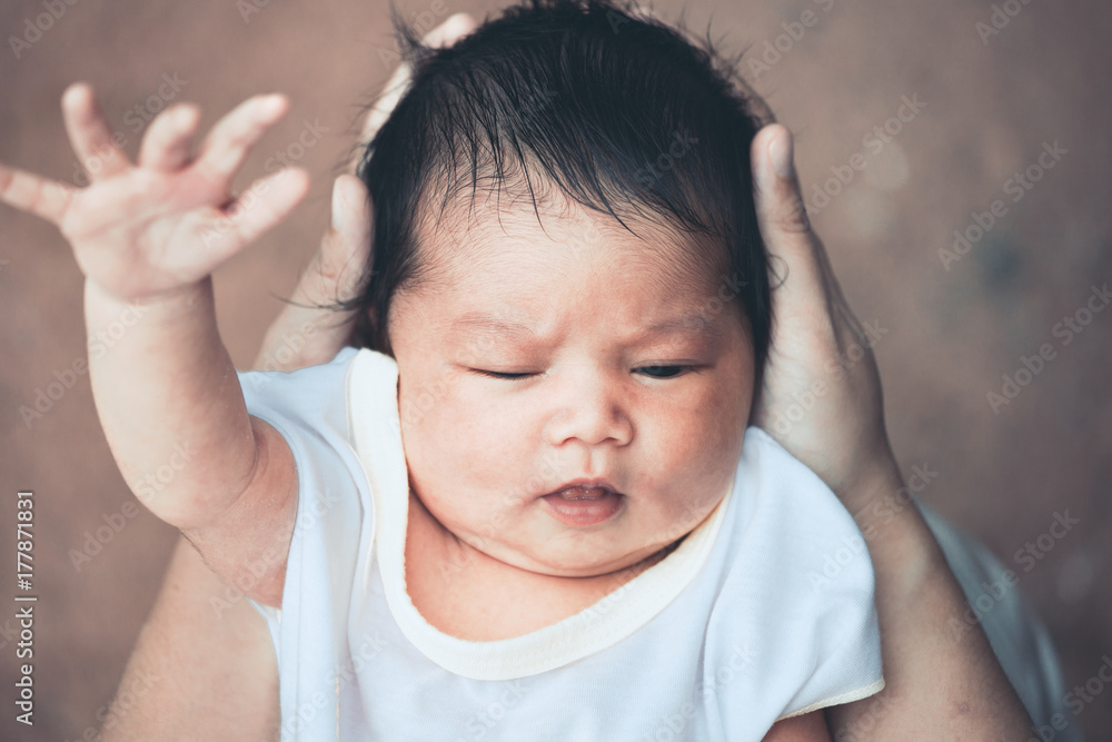 Cute asian newborn baby girl playing with mother. Mother holding head of her baby in hands with tenderness in vintage color tone.