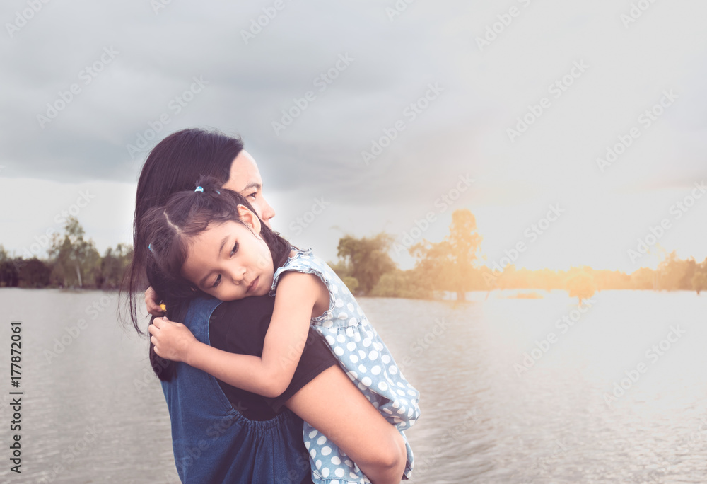 Cute asian little child girl resting on mother's shoulder at riverside in cloudy day Cute asian little child girl resting on mother's shoulder at riverside in cloudy day