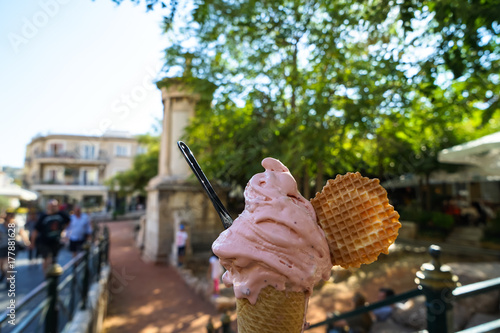 Enjoy sparkled melting pink strawberry ice cream soft serve cone and crispy waffle along sidewalk with blurred people background on sunshine day