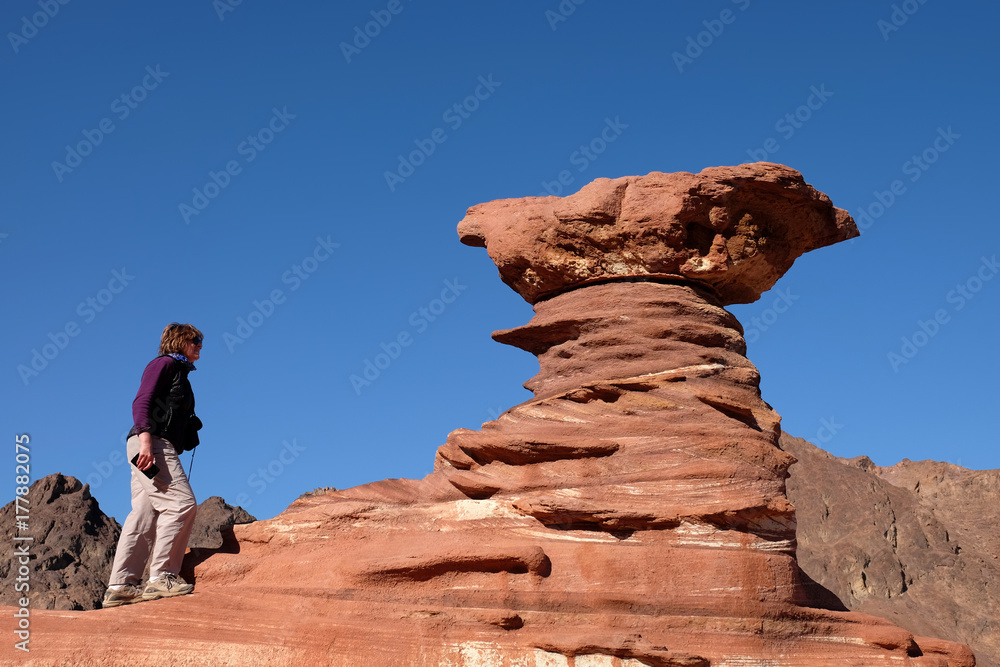 Female hiker ascending on red sandstone mushroom.