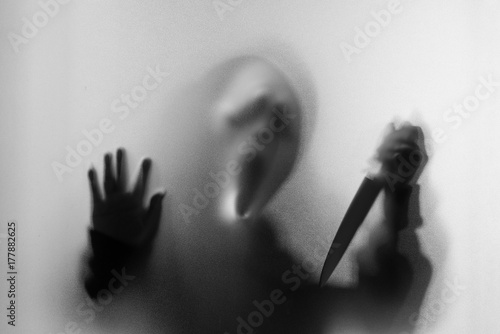 Shadow blur of horror man in screaming mask and show knife in his hand.Dangerous man behind the frosted glass.Mystery man.Black and white picture.Blur picture.Add effects noise and grain.Halloween.