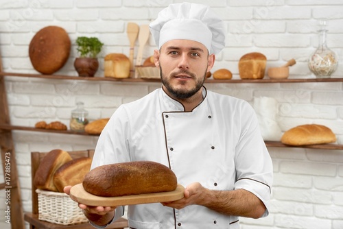 Horizontal shot of a handsome bearded young professional baker in uniform posing at his bakery with a loaf of delicious freshly baked bread profession occupation salesperson small business.