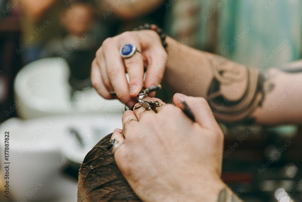 Close up shot of man getting trendy haircut at barber shop. Male hairstylist in tattoos serving client.