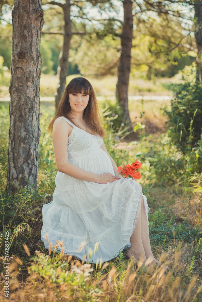 Adorable cute pregnant lady woman in white airy dress posing close to tree in forest holding tummy abdomen dreaming. Attractive beautiful young girl enjoying warm summer with unborn child in belly. Adorable cute pregnant lady woman in white airy dress posing close to tree in forest holding tummy abdomen dreaming. Attractive beautiful young girl enjoying warm summer with unborn child in belly.