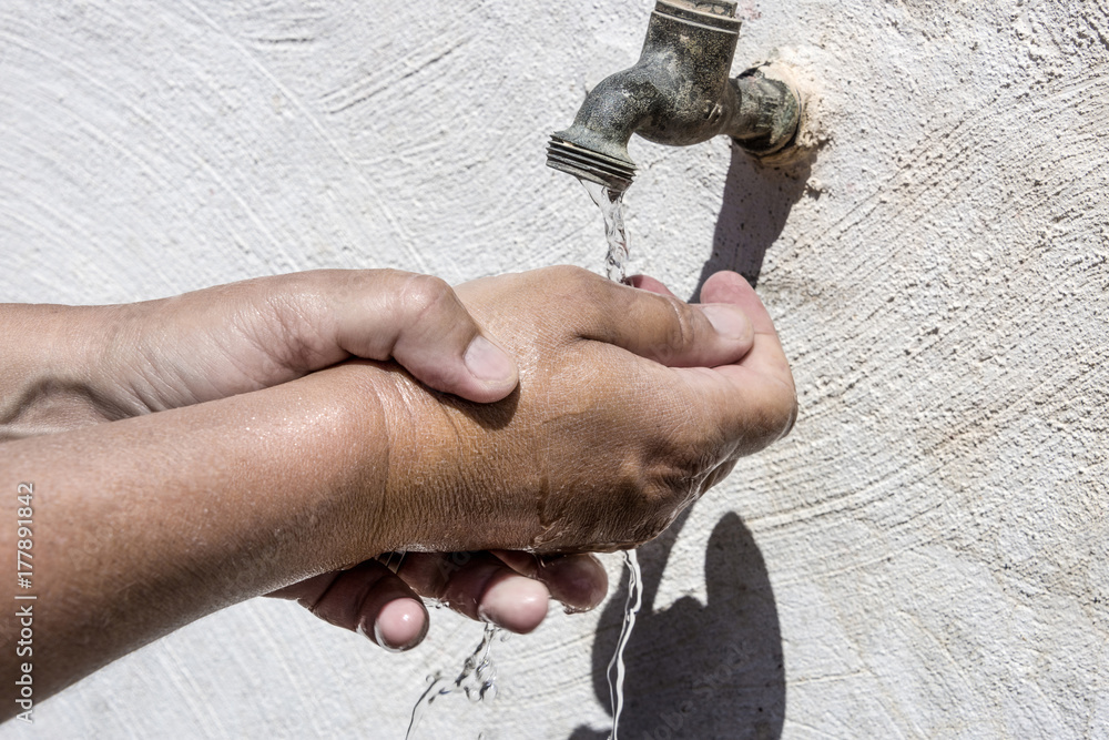 One hand washes the other concept with two hands in running water and an old tap on a white