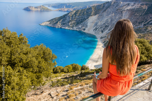 Chica sentada en la valla mirando una playa de Kefalonia (Grecia)