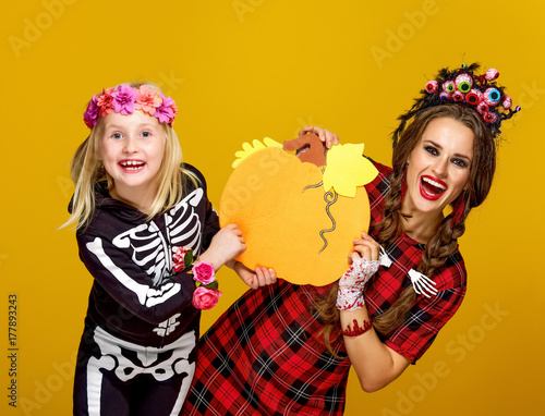 happy mother and child on yellow background showing pumpkin