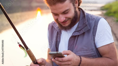 The young hipster fisherman reads sms on a smartphone and smiles. Happy fishman with a phone