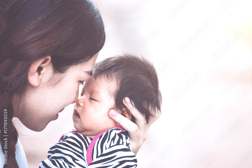 Young asian mother hugging and kissing her newborn baby girl with love in vintage color tone Young asian mother hugging and kissing her newborn baby girl with love in vintage color tone
