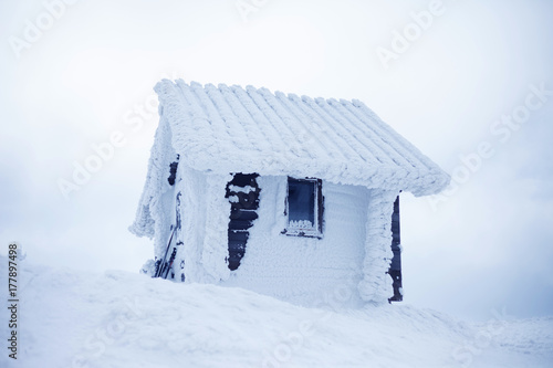 Small wooden house covered with snow and hoarfrost on top of the mountain