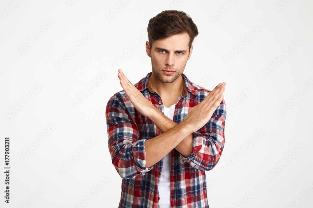 Close-up photo of serious handsome young man showing stop gesture with crossed hands, looking at camera Close-up photo of serious handsome young man showing stop gesture with crossed hands, looking at camera