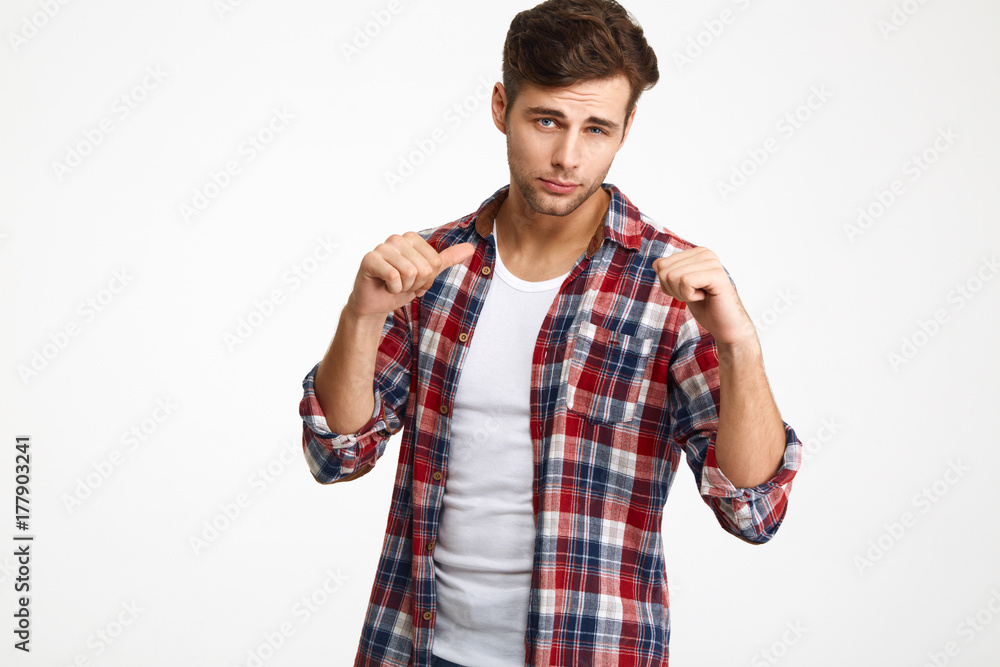Playful handsome young man in checkered shirt showing thumb up gesture, looking at camera Playful handsome young man in checkered shirt showing thumb up gesture, looking at camera