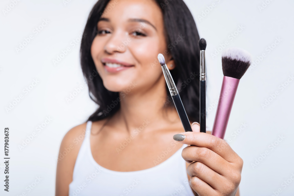 Smiling young woman showing three makeup brushes Smiling young woman showing three makeup brushes