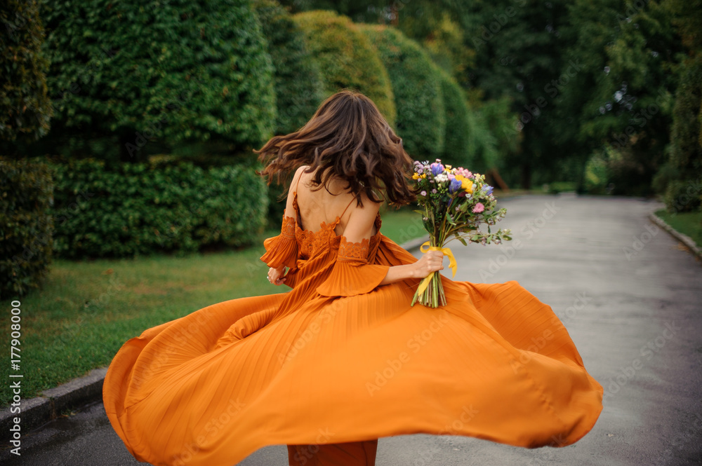 Naklejka premium Back view of attractive woman in long orange dress