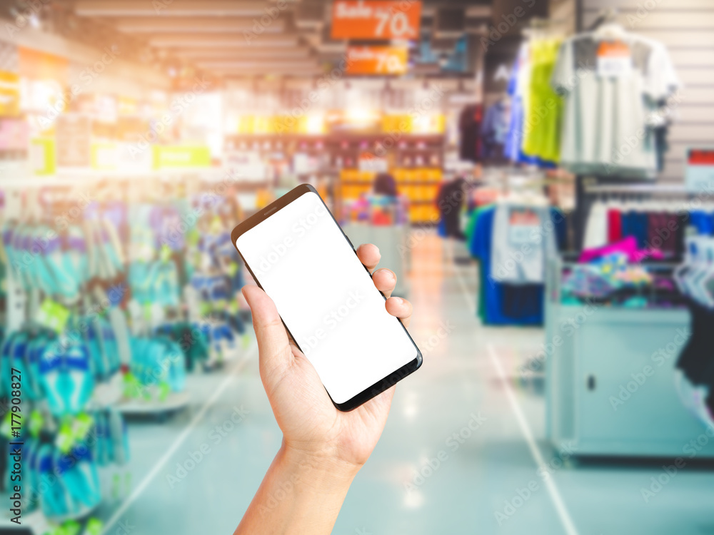 Hand holding smartphone on sport department store background blurred, Shopping centre mall Hand holding smartphone on sport department store background blurred, Shopping centre mall