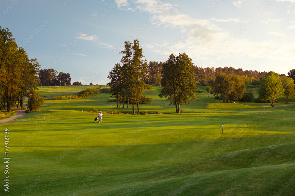 Obraz premium man with his son golfers walking on perfect golf course at summer evening