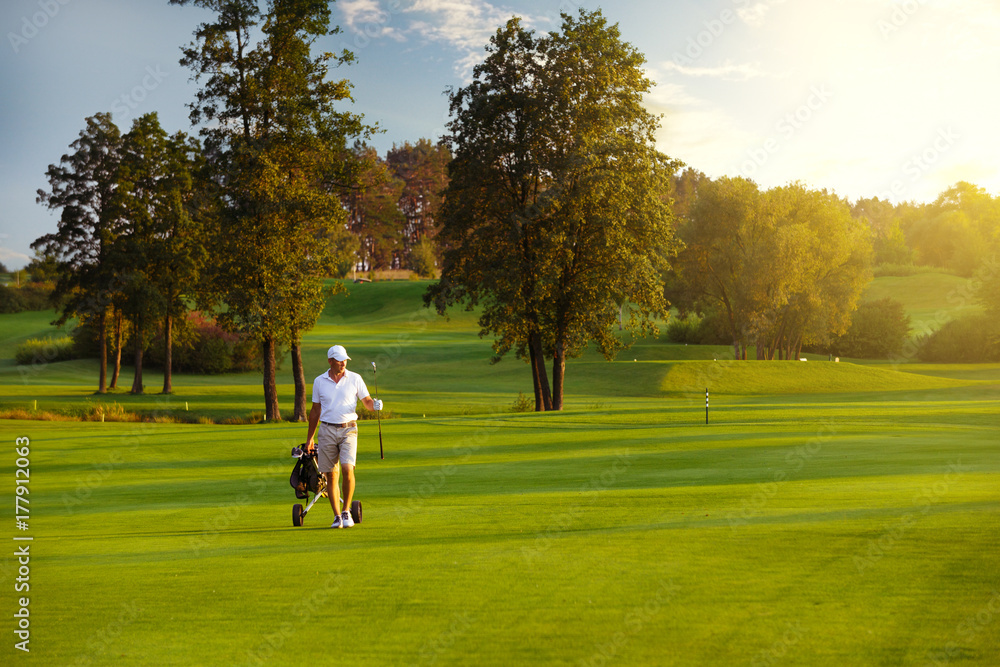 Handsome man golfer walking on fairway at golf course in the summer evening Handsome man golfer walking on fairway at golf course in the summer evening