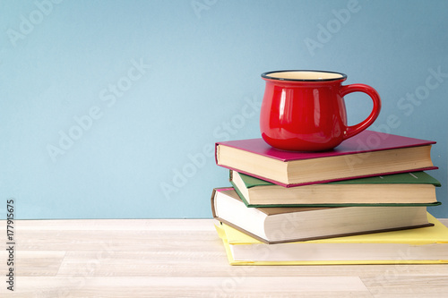 Stack of books and red mug against blue background. Copy space for text.