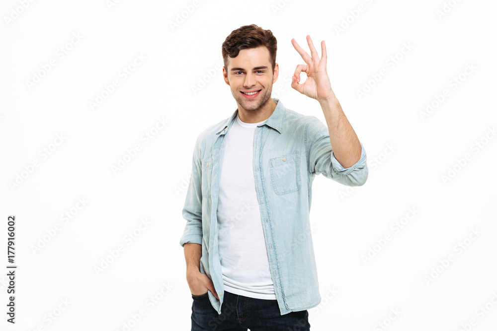 Portrait of a smiling young man standing and showing ok Portrait of a smiling young man standing and showing ok