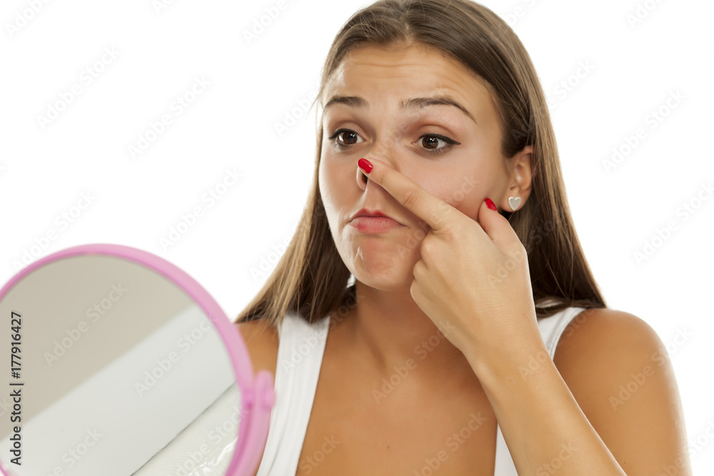 young woman looking at herself in the mirror and touching her nose young woman looking at herself in the mirror and touching her nose