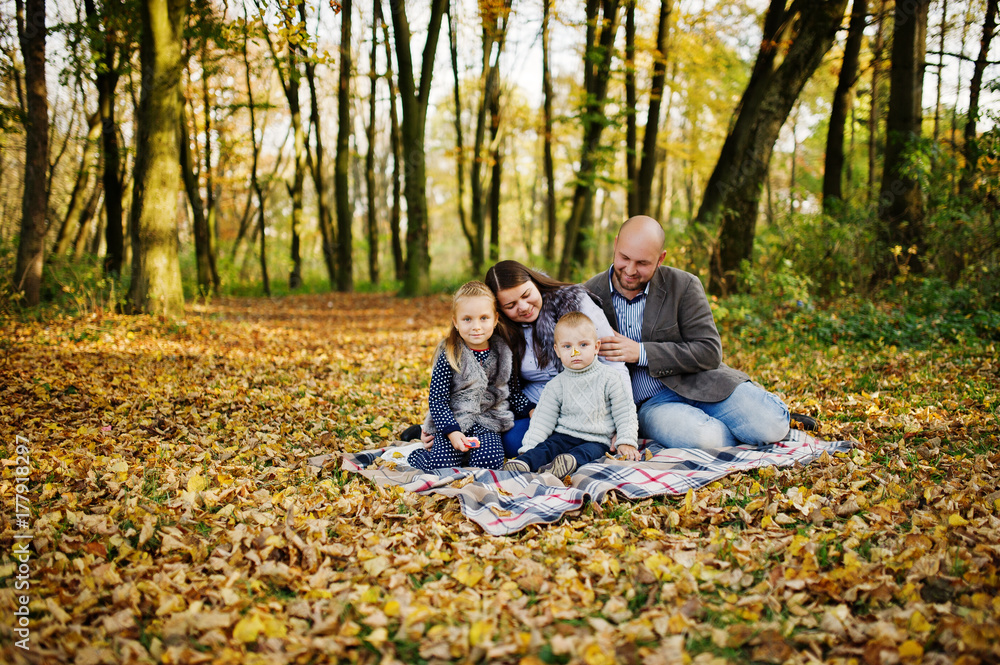 Happy caucasian family of mom dad and little girl with boy sitting on plaid at majestic autumn fall forest. Happy caucasian family of mom dad and little girl with boy sitting on plaid at majestic autumn fall forest.