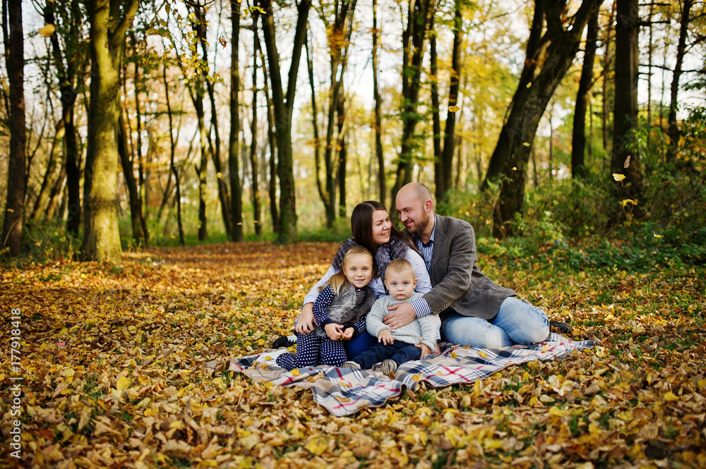 Happy caucasian family of mom dad and little girl with boy sitting on plaid at majestic autumn fall forest. Happy caucasian family of mom dad and little girl with boy sitting on plaid at majestic autumn fall forest.