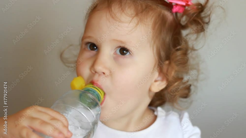Funny cute little girl is drinking water from a bottle. Child and thirst. The baby takes a sip of the drink close up. Funny cute little girl is drinking water from a bottle. Child and thirst. The baby takes a sip of the drink close up.