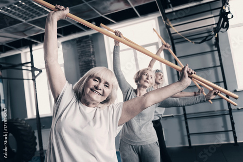Cheerful women doing stretching with wooden exercise sticks