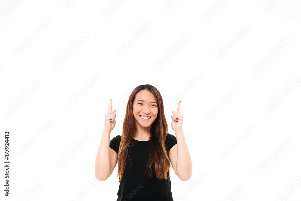 Young cheerful asian girl in black tshirt pointing with two fingers upward, looking at camera Young cheerful asian girl in black tshirt pointing with two fingers upward, looking at camera