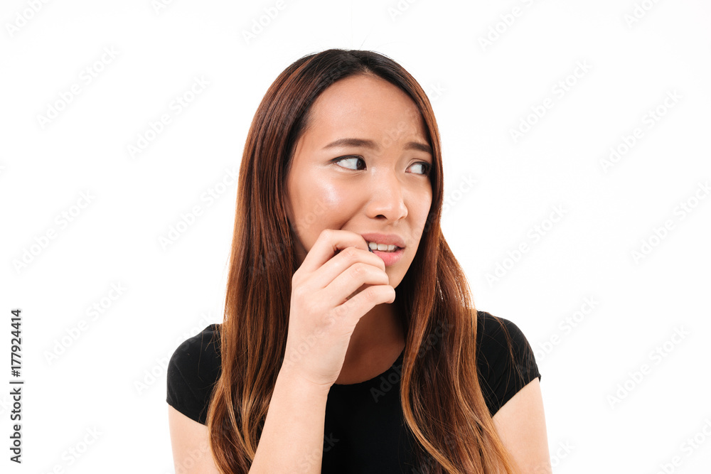 Close-up portrait of scared young asian woman standing with finger in her mouth, lookin aside Close-up portrait of scared young asian woman standing with finger in her mouth, lookin aside