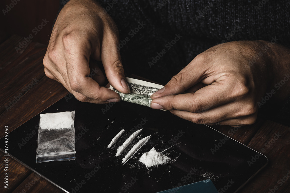 Man hands rolls dollar banknote for using cocaine powder lines, Drug addiction