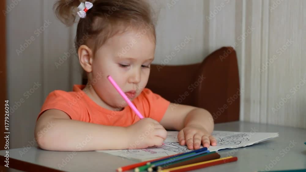 An amusing pretty girl sits at a table and draws in multicolored pencils. Child and creativity. An amusing pretty girl sits at a table and draws in multicolored pencils. Child and creativity.