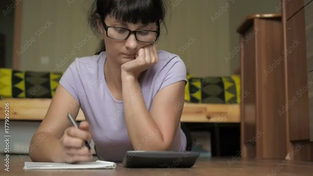 Young woman with glasses with notebook and calculator studying in college. Business woman working with calculator. Budget, finances - woman with papers and calculator counting money at home Young woman with glasses with notebook and calculator studying in college. Business woman working with calculator. Budget, finances - woman with papers and calculator counting money at home