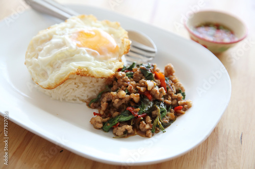 stir fried pork and basil with rice and egg on wood background thai food